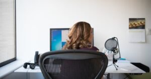 Adult woman working in a contemporary office setting with computer and microphone.