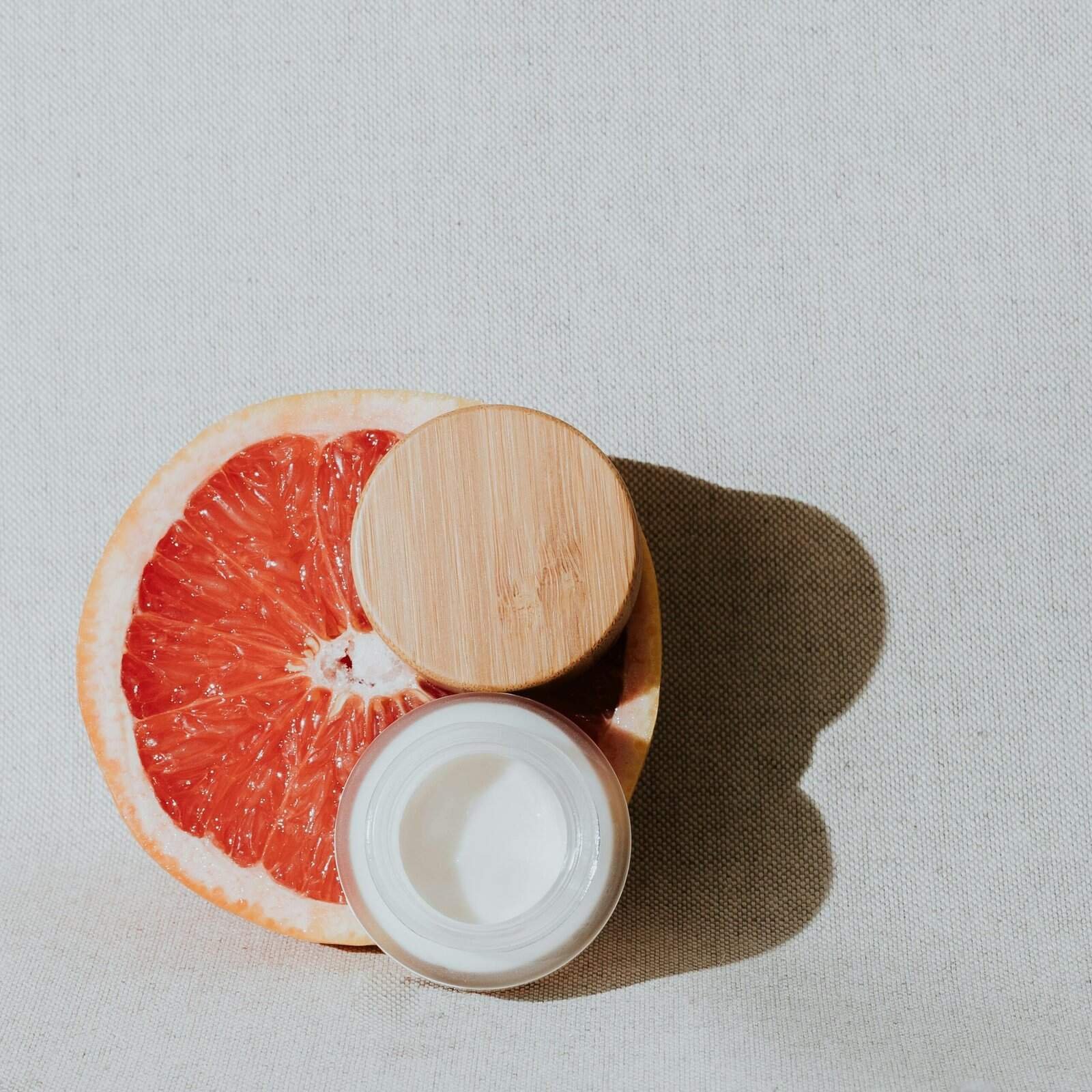 Fresh grapefruit half with skincare cream on wooden tray, natural skincare concept.