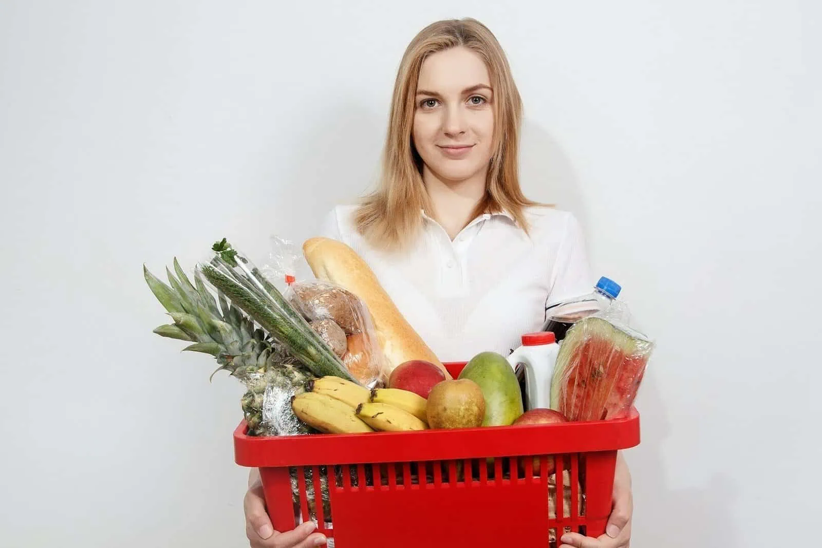 Young woman holding a shopping basket filled with fresh fruits and vegetables.