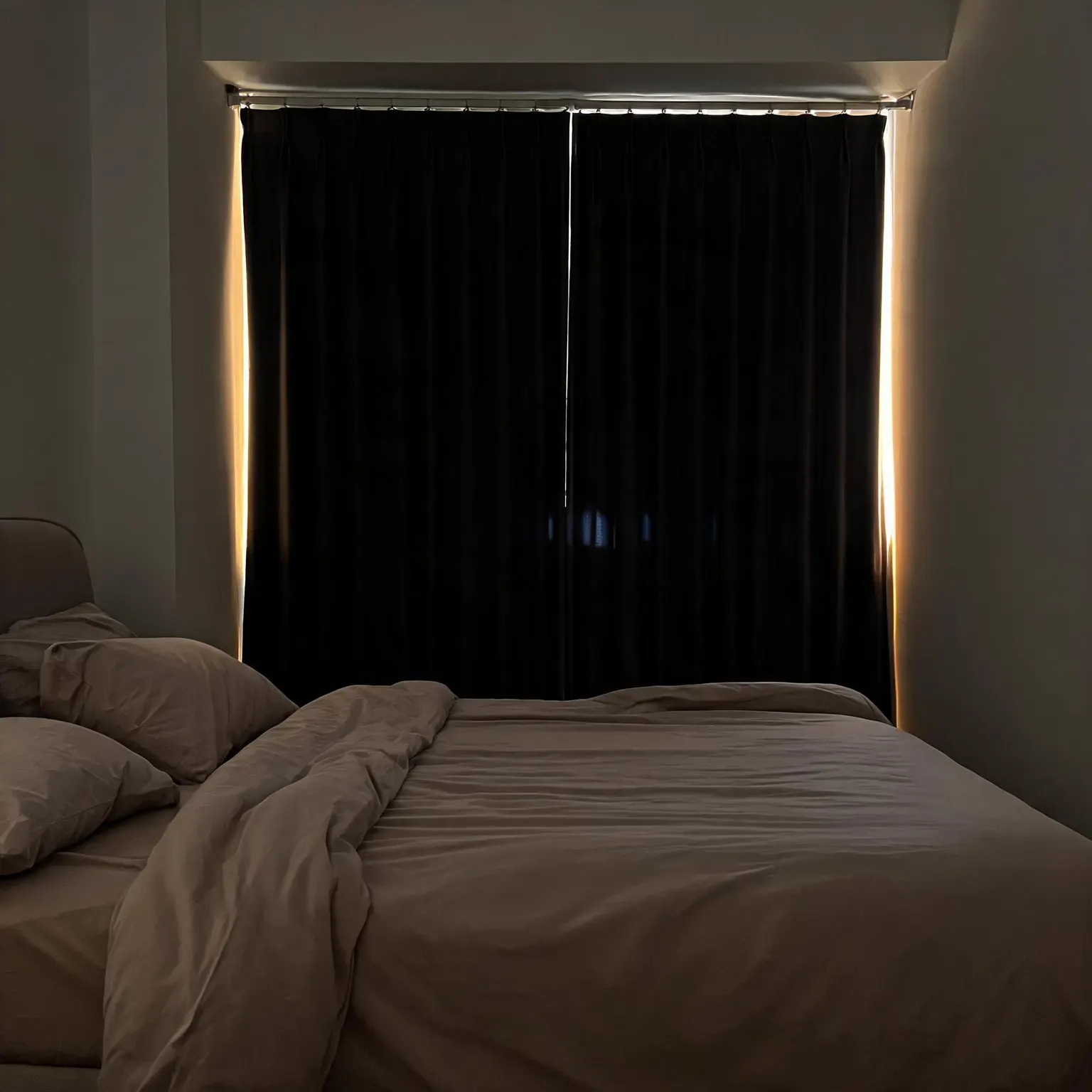 Best blackout curtains of 2026: floor-length charcoal blackout curtains blocking all but a thin golden rim of light in a serene dark bedroom at dawn