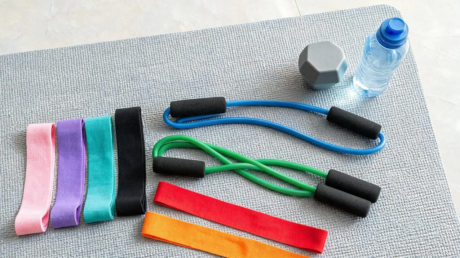 Set of colorful resistance bands, water bottle, and gym accessories for workout.