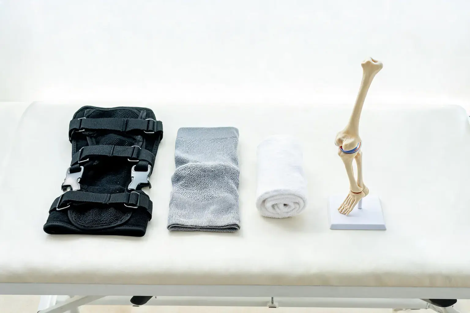 Hinged knee brace and knitted compression knee sleeve on a white physical therapy table with a towel and anatomical knee model - best knee brace for arthritis 2026